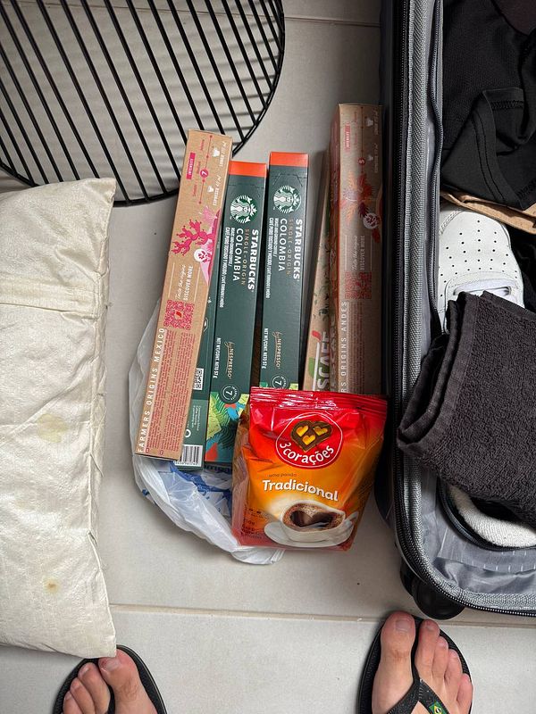 The image features coffee products packed in a suitcase alongside casual clothing and a pillow.