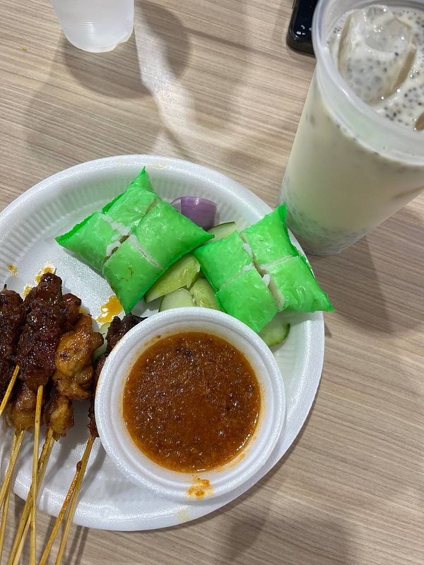 A plate of satay with green rice cakes and a drink.