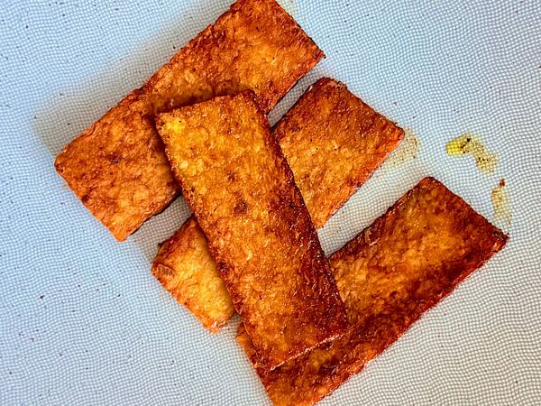 A close-up photo of a cluster of fresh tempeh pieces on a wooden surface.