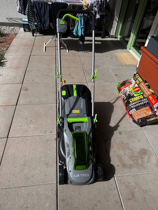 A lawnmower is positioned on a patio with laundry hanging in the background.