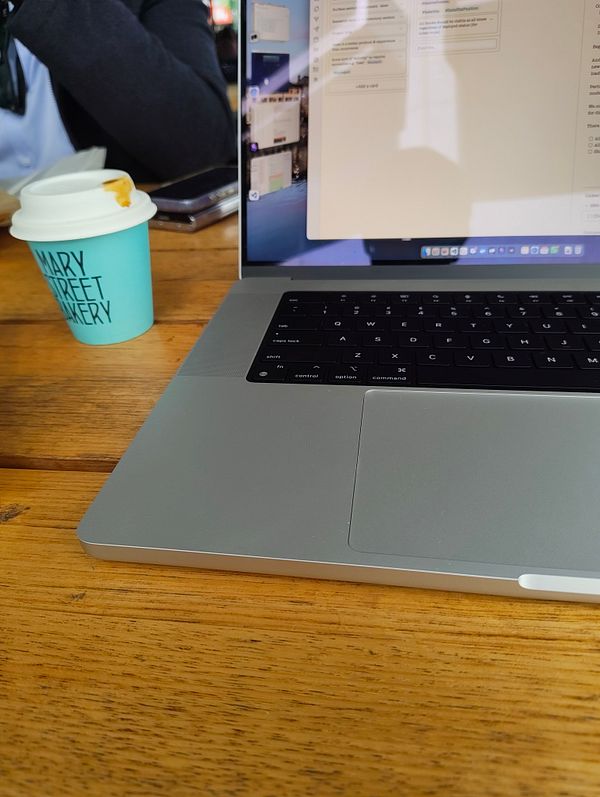 A laptop is positioned on a wooden table next to a coffee cup from Mary Street Bakery.