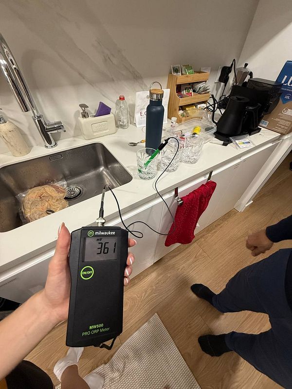A person is holding a Milwaukee MW500 PRO ORP meter displaying a reading of 361 mV in a kitchen setting.