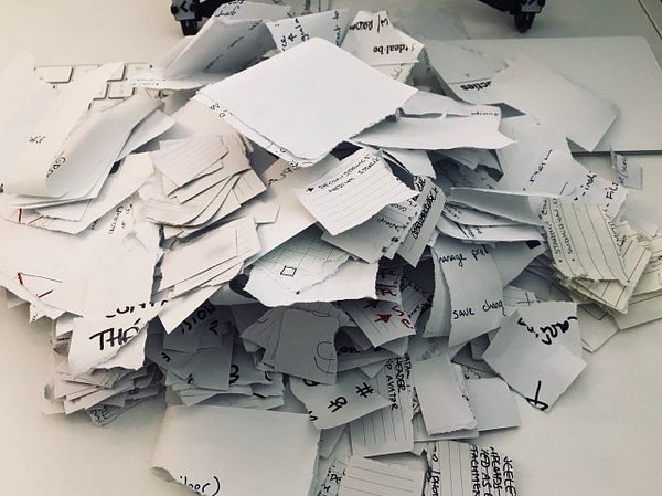 The image shows a pile of torn index cards with handwritten notes on them.