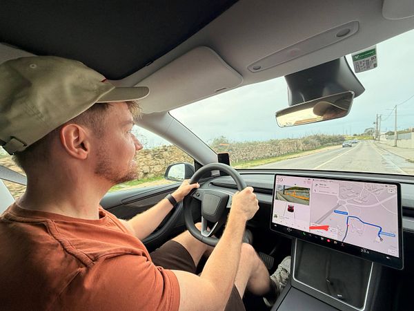 Photo of an orange and white cat lying on a bed with grey sheets, looking towards the camera.