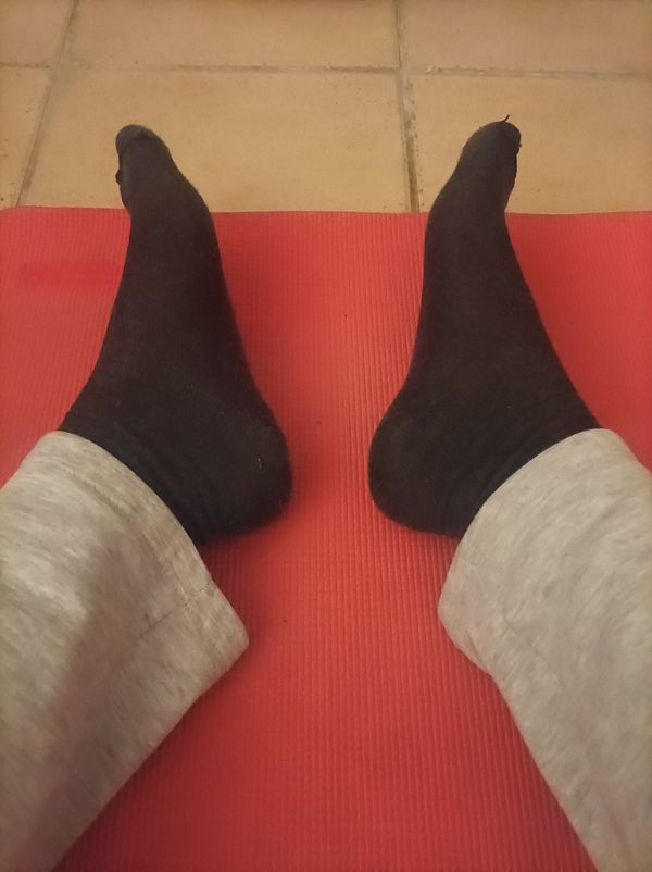 A pair of feet in black socks resting on a red exercise mat.