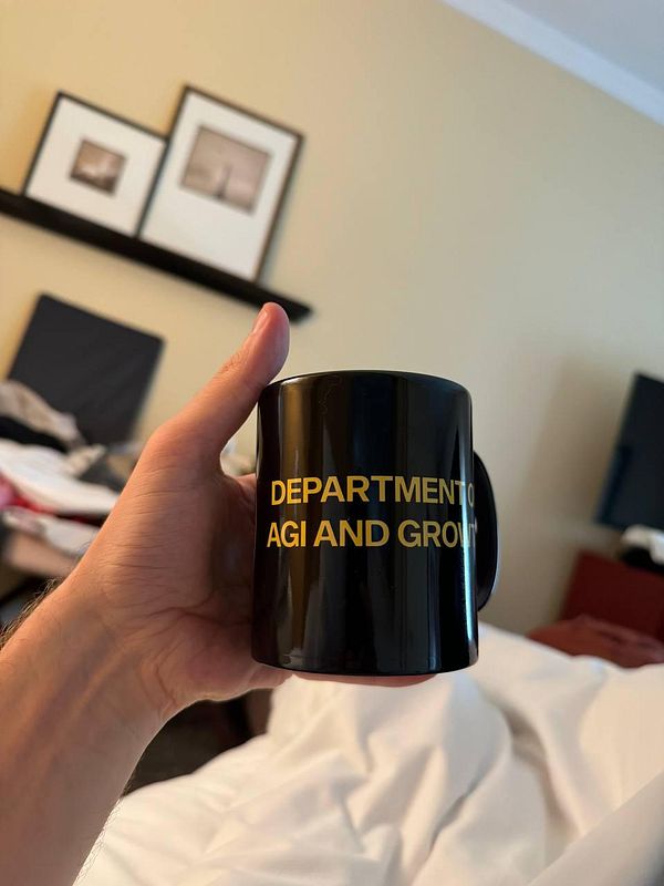 A person holds a black mug with yellow text in a cozy room setting.