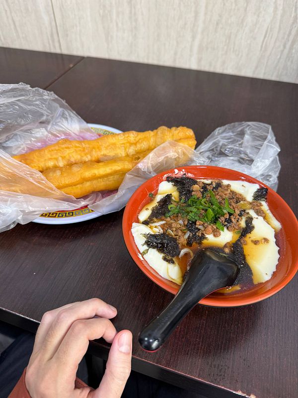 Photo of a breakfast meal with steamed buns and a side dish on a wooden table in a casual dining setting.