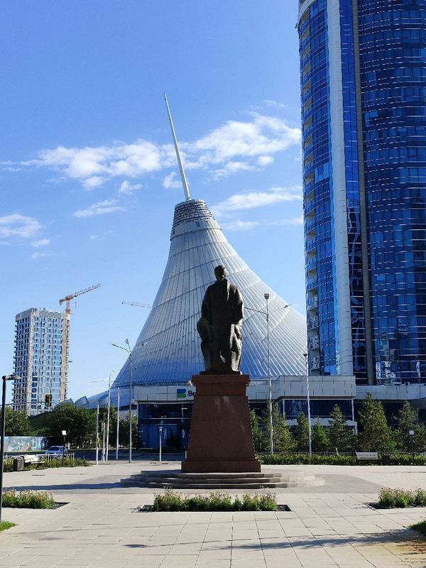 A statue stands prominently in front of a modern architectural structure in Astana.
