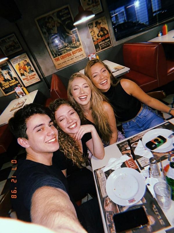 A group of four friends poses for a selfie in a lively diner setting.