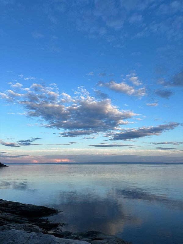 A serene view of a calm body of water under a blue sky with scattered clouds.