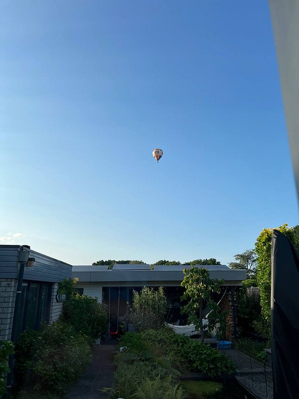 A colorful hot air balloon floats in a clear blue sky above a residential area.
