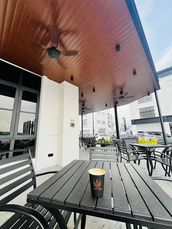 A coffee cup sits on a black wooden table in an outdoor café setting.