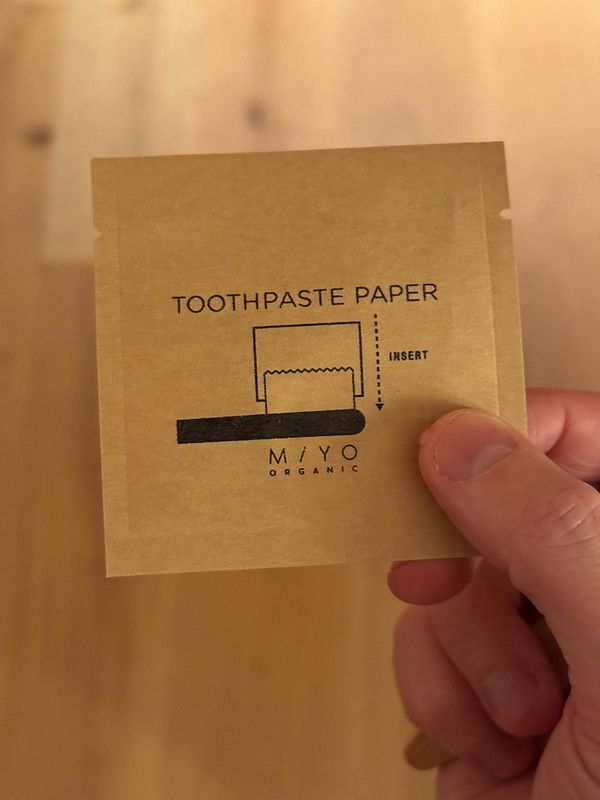 A person holds a packet of eco-friendly toothpaste paper labeled 'TOOTHPASTE PAPER'.