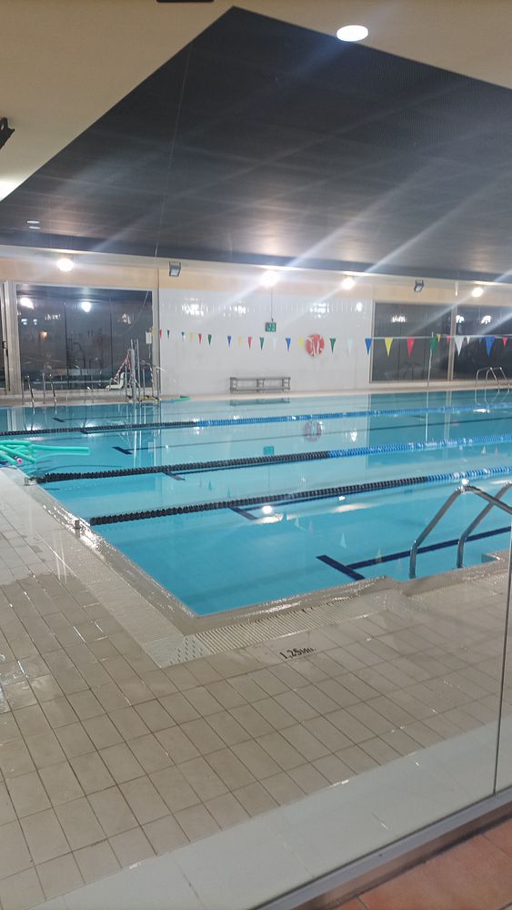 An indoor swimming pool with clear water and lane markings, illuminated by overhead lights.