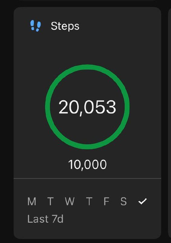 A person walking on a long paved road lined with trees and buildings under a bright sky.