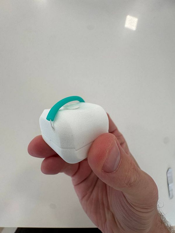 A person is holding a small, white device with a green handle.