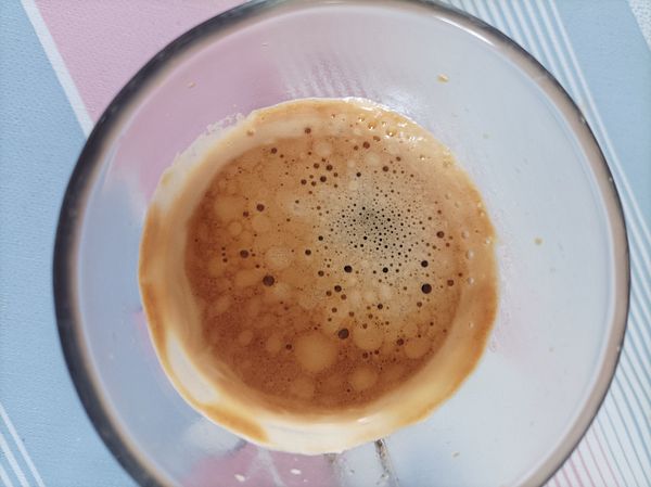 A close-up view of a glass containing espresso with a rich crema on top.