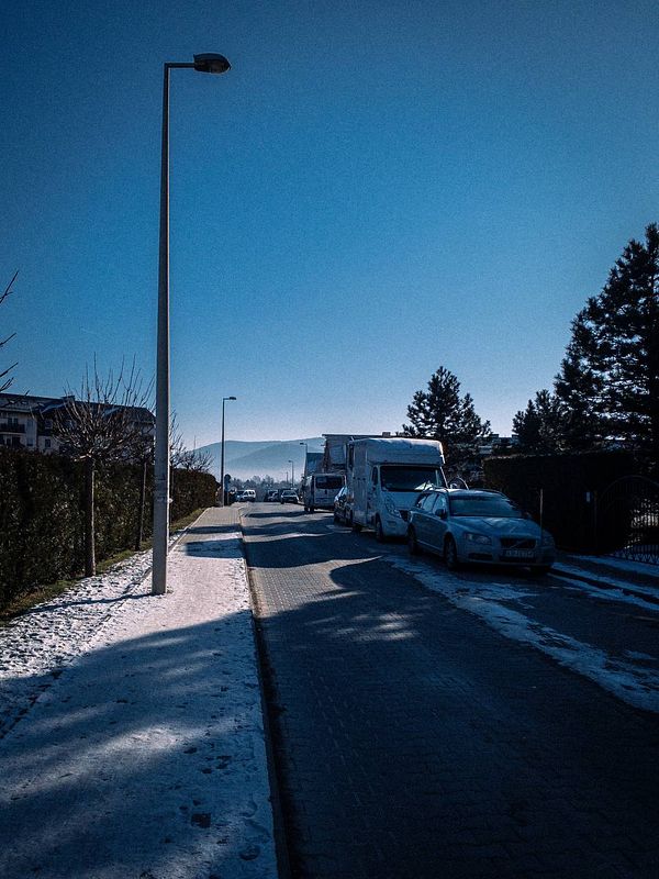A serene morning scene featuring a snow-covered street lined with parked cars and a clear blue sky.