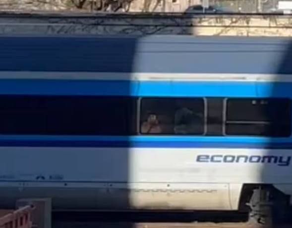 A person is waving at their wife from a train platform as the train approaches.