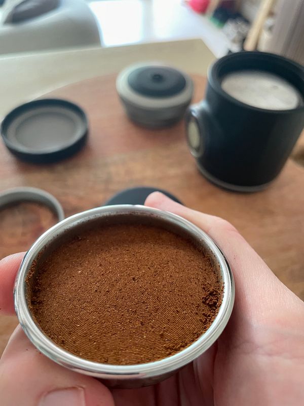 A close-up of freshly ground coffee in a metal portafilter, held in a hand.