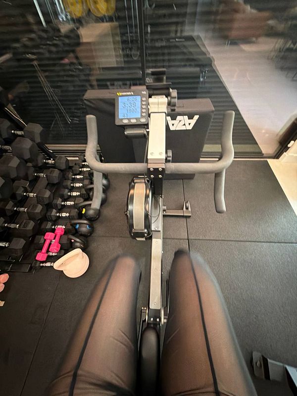 A person wearing workout gear is exercising inside a gym using a rowing machine.