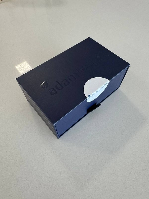 A sleek, dark blue box labeled with the brand 'adamhealth' is placed on a smooth, light-colored surface.