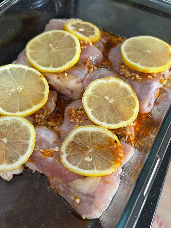A pot cooking lemon chicken with broccoli is on a stovetop heat burner next to a grilled chicken arm on a plate.