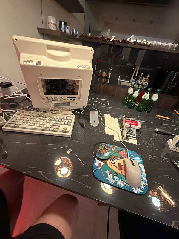 A retro computer setup is displayed on a table, featuring a disassembled monitor and various tech components.