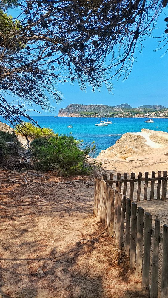 A scenic coastal view featuring a tranquil blue sea, rocky shoreline, and a wooden fence.