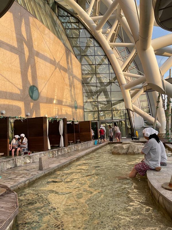 The image depicts a serene spa environment featuring a shallow pool and wooden treatment areas.