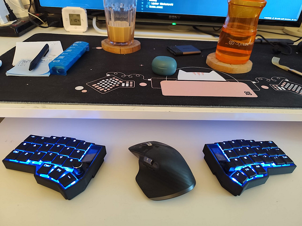 A workspace featuring a split keyboard, a mouse, and various items on a desk.