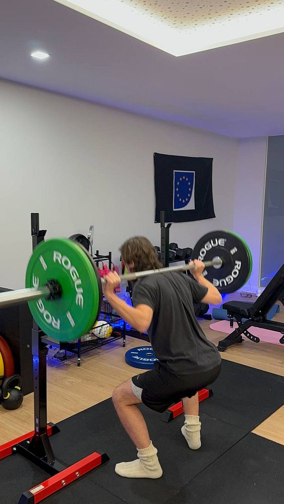 A person is performing a squat with a barbell in a home gym setting.