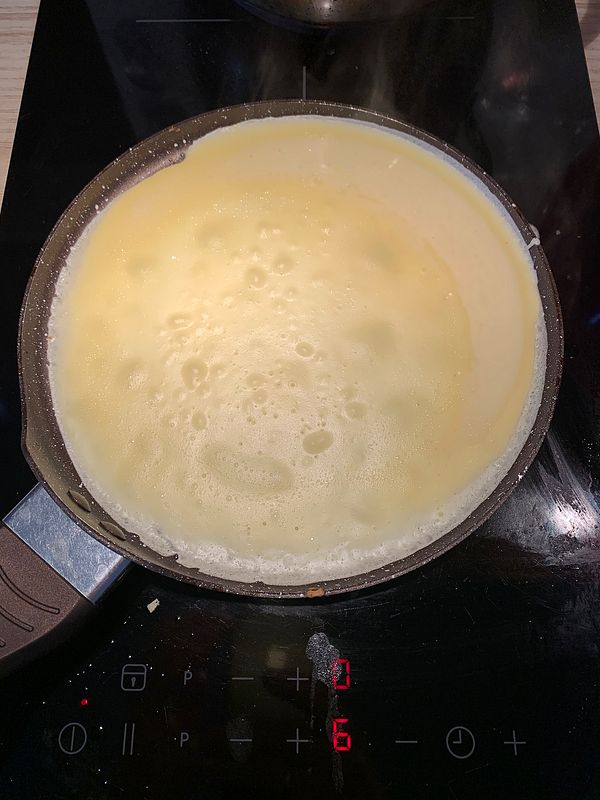 A frying pan with crepe batter cooking on an induction stove.