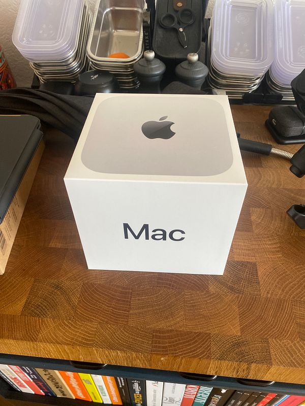 Photo of a Mac Mini device on a wooden table with a box and accessories.