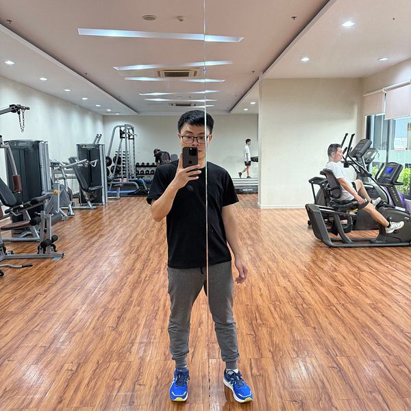 A person stands in a gym, taking a selfie in front of a mirror.