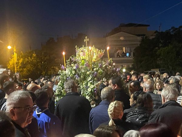 A large crowd gathers around a floral arrangement during a nighttime procession.
