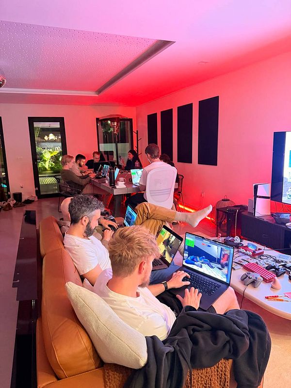 A group of people working and gaming together in a modern coworking space with red ambient lighting.