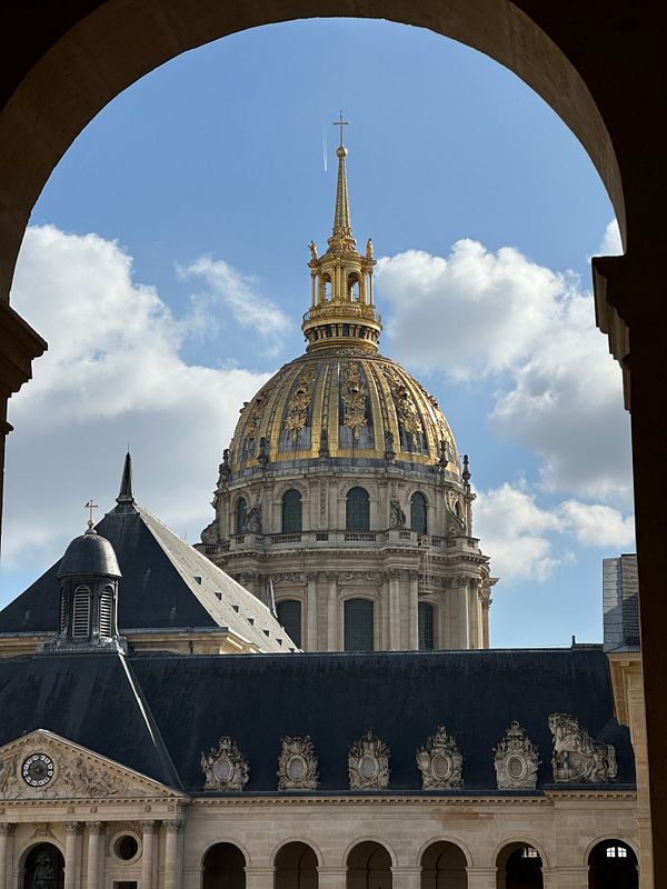 The image captures the golden dome of the Invalides Museum framed by an archway.