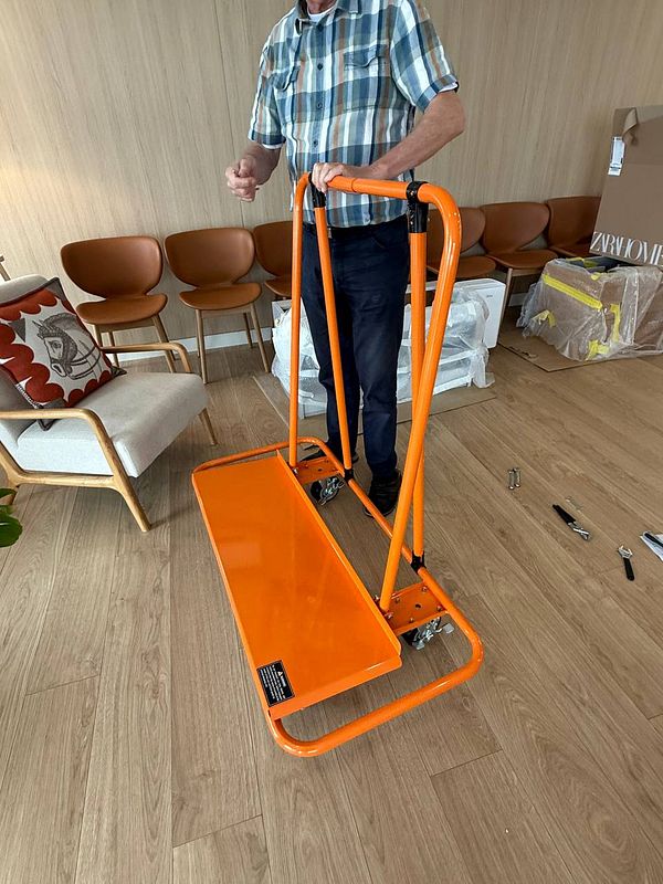 A person is assembling a bright orange carriage designed for heavy lifting.