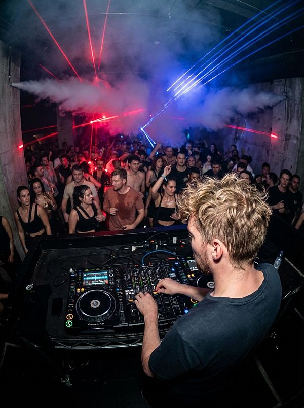 A DJ performs in front of an energetic crowd at a vibrant electronic music event.