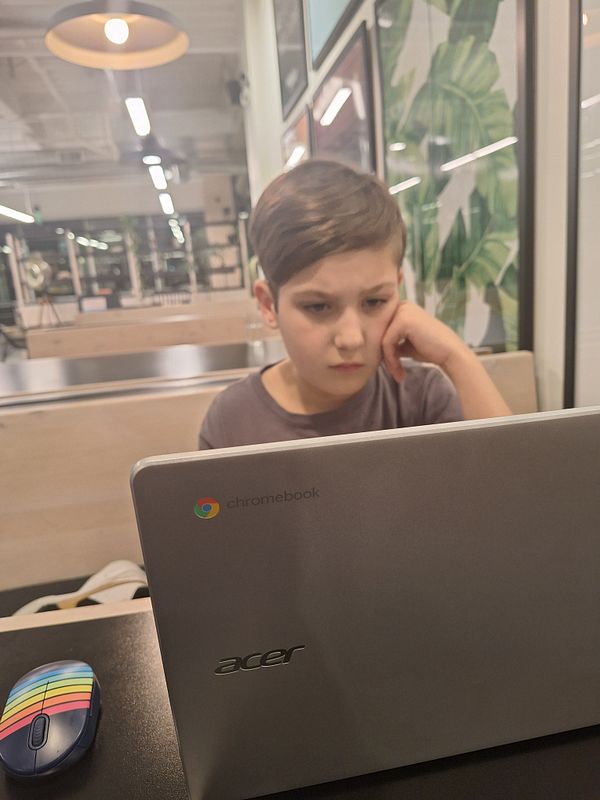 A young boy is intently watching a show on a Chromebook in a modern café setting.