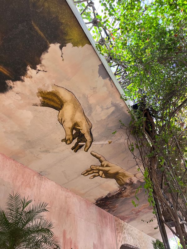 A mural depicting two hands reaching towards each other is surrounded by lush greenery.