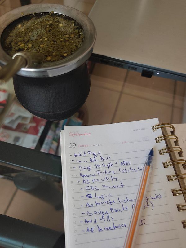 A glass table with a mate gourd, a laptop, and a spiraled planner opened to Monday, September 28, with handwritten tasks and a pen.