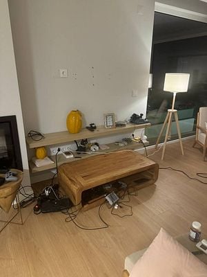 A living room setup with a wooden coffee table, various electronic devices, and a wall with mounting holes.