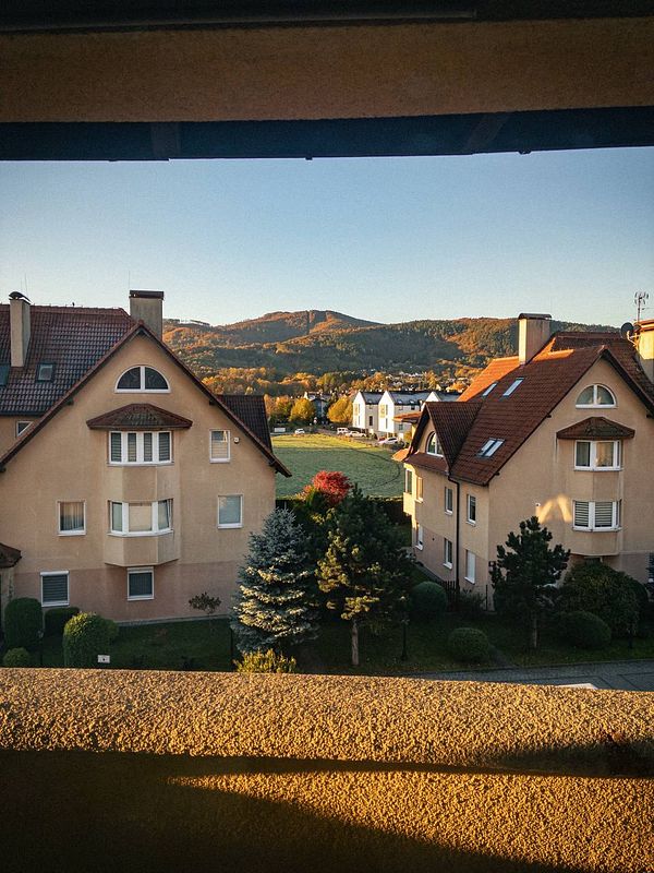 A serene morning view from a window showcasing residential buildings and a mountainous landscape.