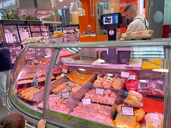 A bustling butcher shop display filled with various types of meat and a customer interacting with the butcher.