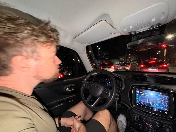 A nighttime cityscape in Brazil featuring illuminated streets, buildings, and a prominent bridge with cables glowing against a dark sky.