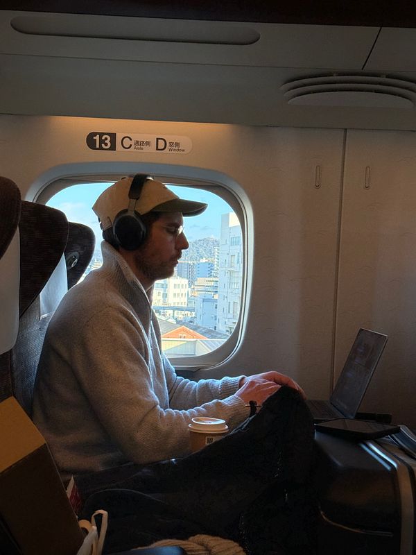 A person is working on a laptop while sitting on a train, with a view of the city outside the window.