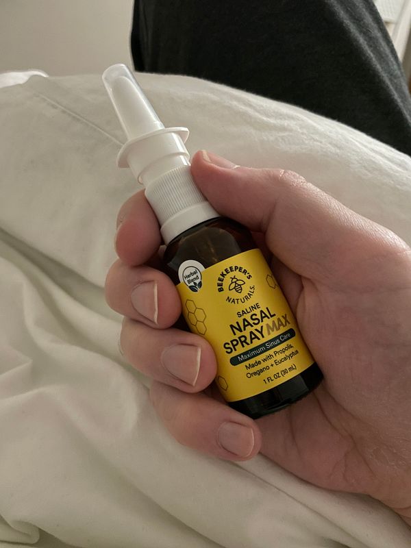 A person holds a bottle of nasal spray while resting on a bed.