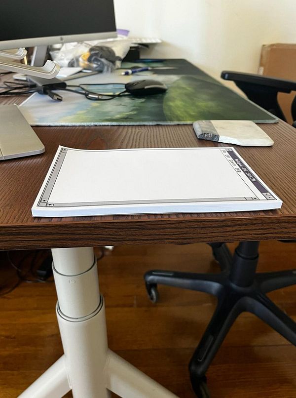 A notepad with a design inspired by NOTEPAD.EXE is placed on a wooden desk.